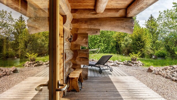A wooden deck with a bench and a lounge chair, surrounded by a natural landscape and a body of water. - Chalet "Weiss" with Mountain Views, Private Garden, and Wi-Fi (Wörgl)