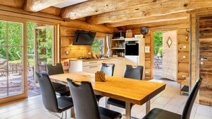 A wooden cabin interior with a dining area, kitchen, and large windows. - Chalet "Weiss" with Mountain Views, Private Garden, and Wi-Fi (Wörgl)