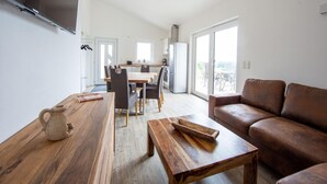 A modern living space with a wooden dining table, a brown leather sofa, and a kitchen in the background. - Ferienwohnungen in Filz in der Eifel (Filz)