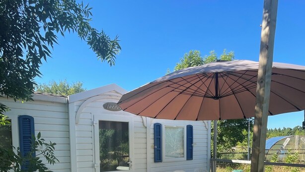A wooden deck with a table and chairs, a covered area with an umbrella, and a white building with blue shutters.
