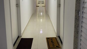 Un pasillo de hotel con paredes blancas, piso de baldosas y una puerta al final.