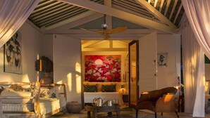 A cozy room with a ceiling fan, a sofa, a chair, a table with a tray, and a large painting on the wall. - Private oceanfront retreat in Jericoacoara with luxury suites (Jijoca de Jericoacoara)