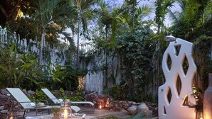 A wooden deck with lounge chairs, a table with candles, and a decorative wall with hanging plants. - Private oceanfront retreat in Jericoacoara with luxury suites (Jijoca de Jericoacoara)