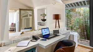 A modern workspace with a desk, laptops, a phone, and a chair. There is a large mirror, a potted plant, and a view of greenery outside. - Private oceanfront retreat in Jericoacoara with luxury suites (Jijoca de Jericoacoara)