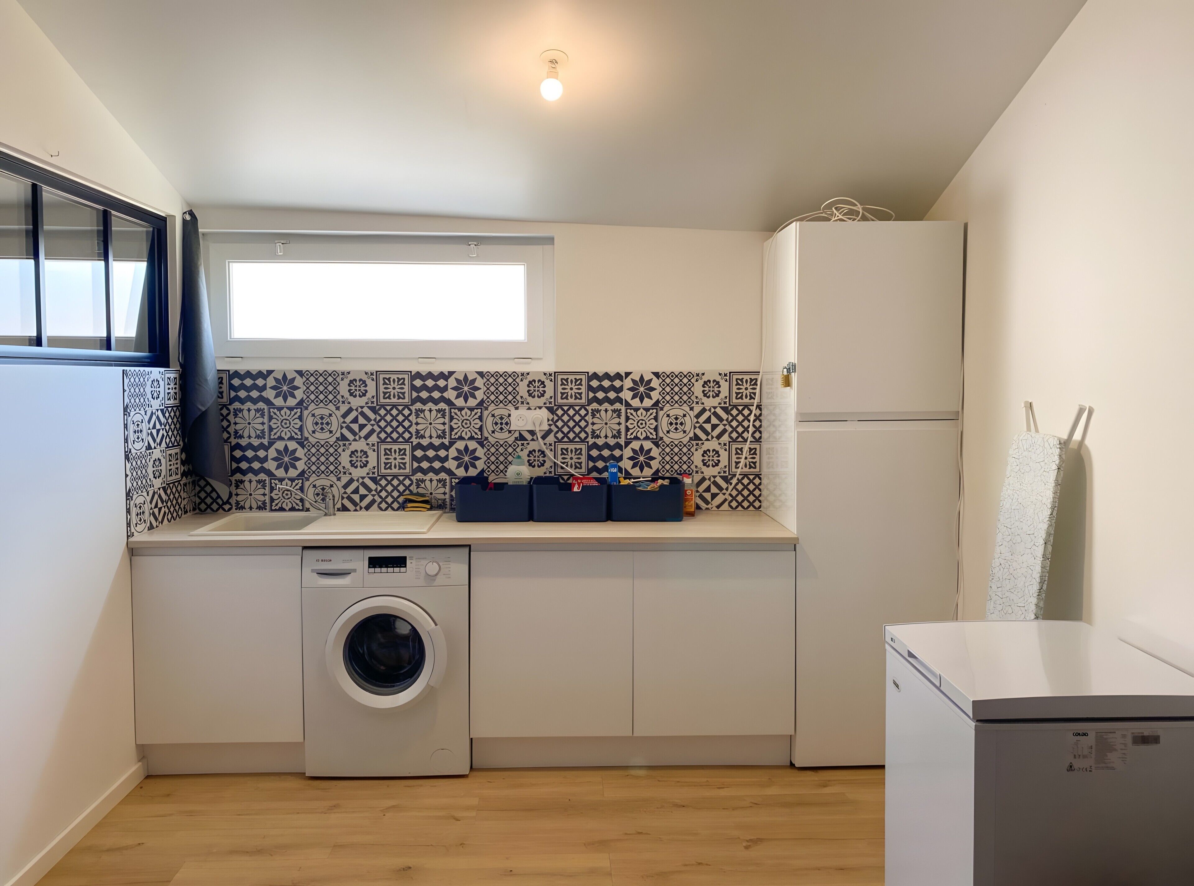 Ett kompakt kök med tvättmaskin, kylskåp och ett fönster med gardiner.