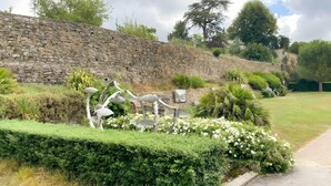 Un muro de piedra, una escultura de metal y un jardín cuidado con un sendero pavimentado.