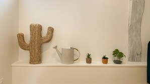 Una estantería blanca con un cactus tejido grande, un regador de metal y tres pequeñas macetas.