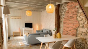 Una sala moderna con sofá, televisor, mesa de comedor, sillas e iluminación colgante.