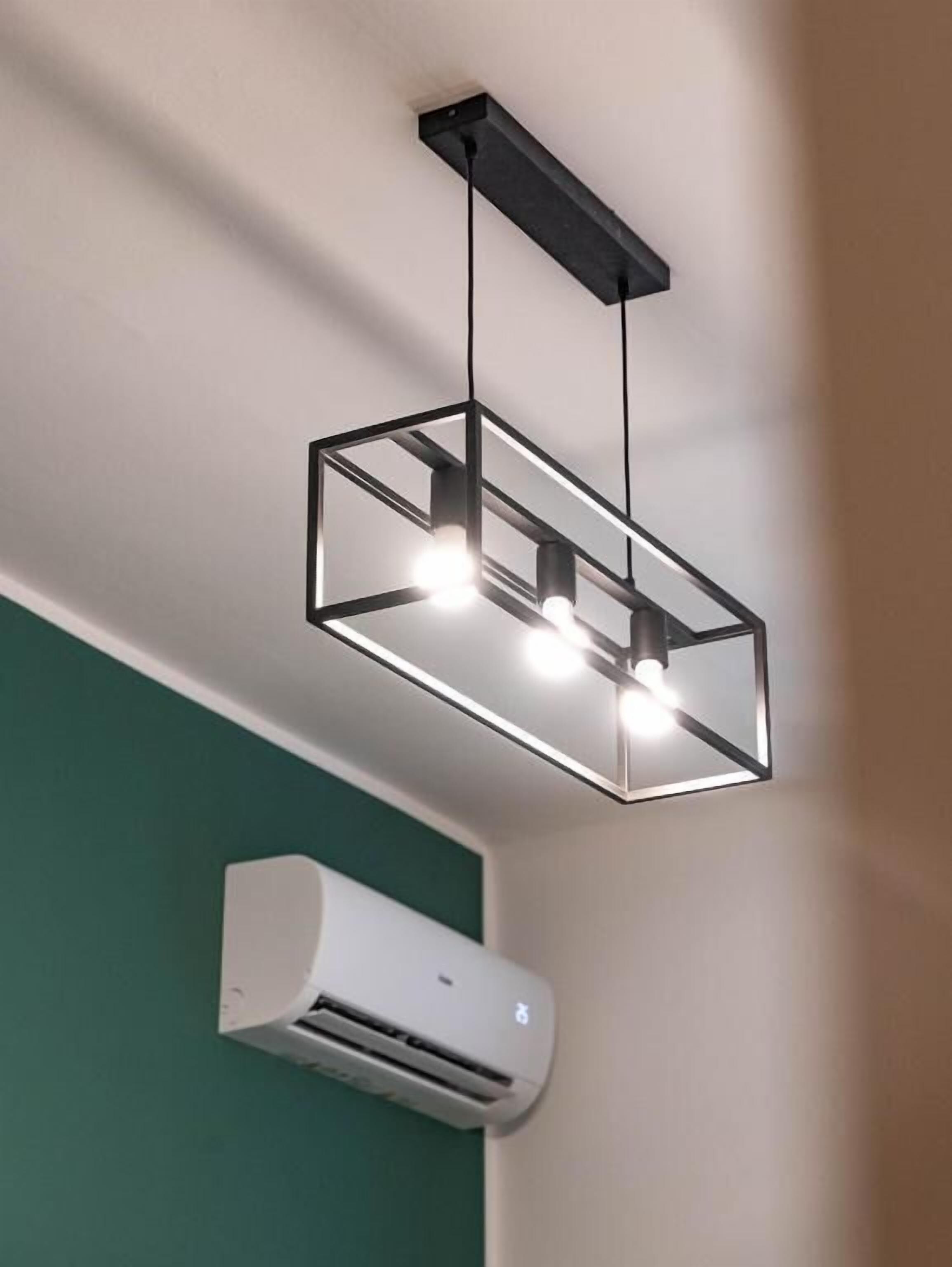 A modern ceiling light fixture with three bulbs and an air conditioning unit mounted on the wall.