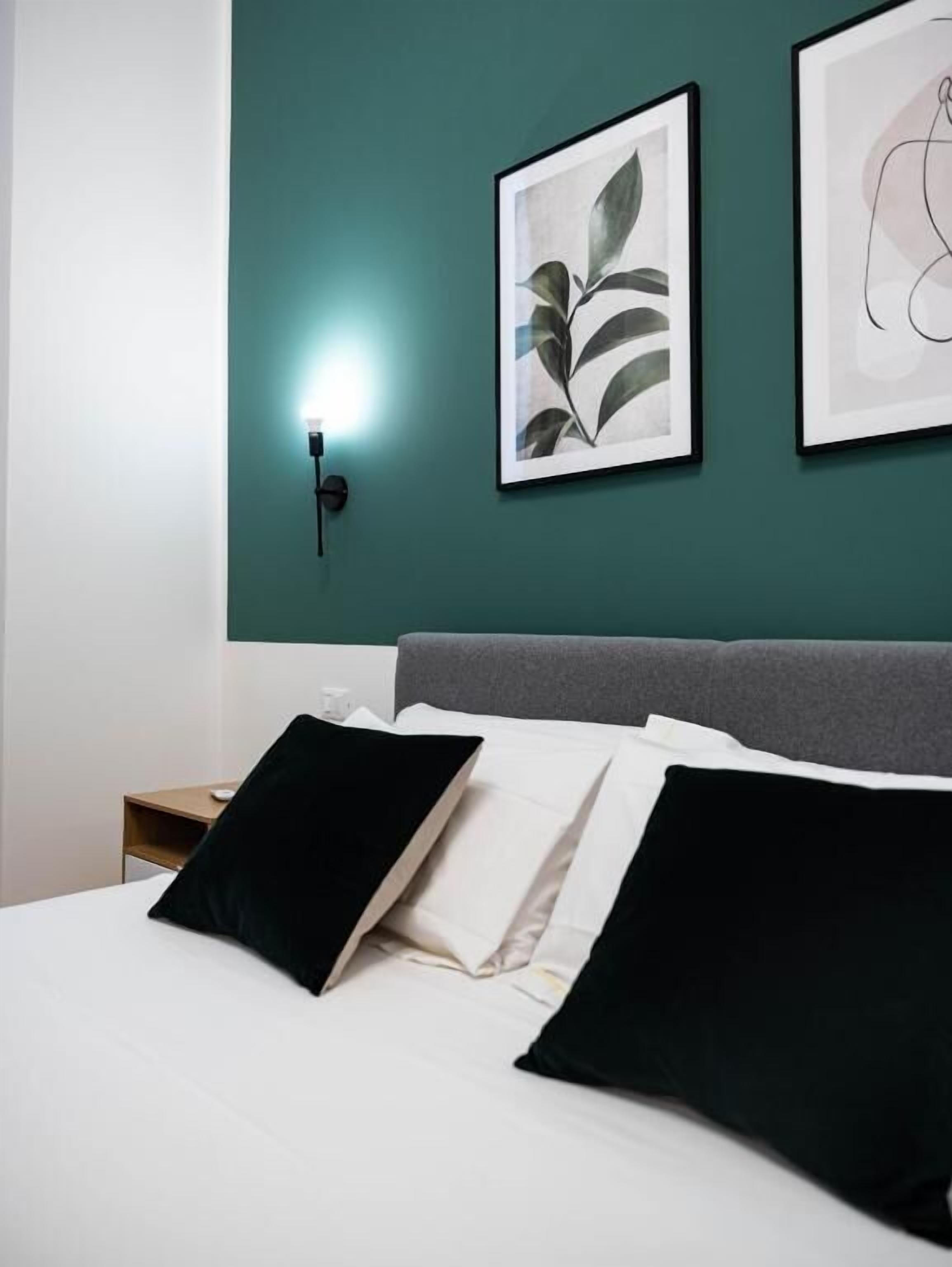A hotel room with a bed, two framed artworks on the wall, a bedside table, and a nightstand.