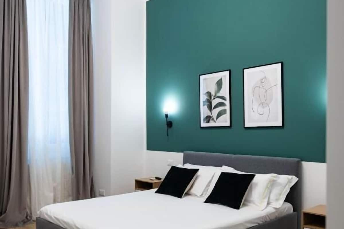 Ein modernes Schlafzimmer mit einem Bett, zwei Nachttischen, einem Beistelltisch und einem Fenster mit Vorhängen.