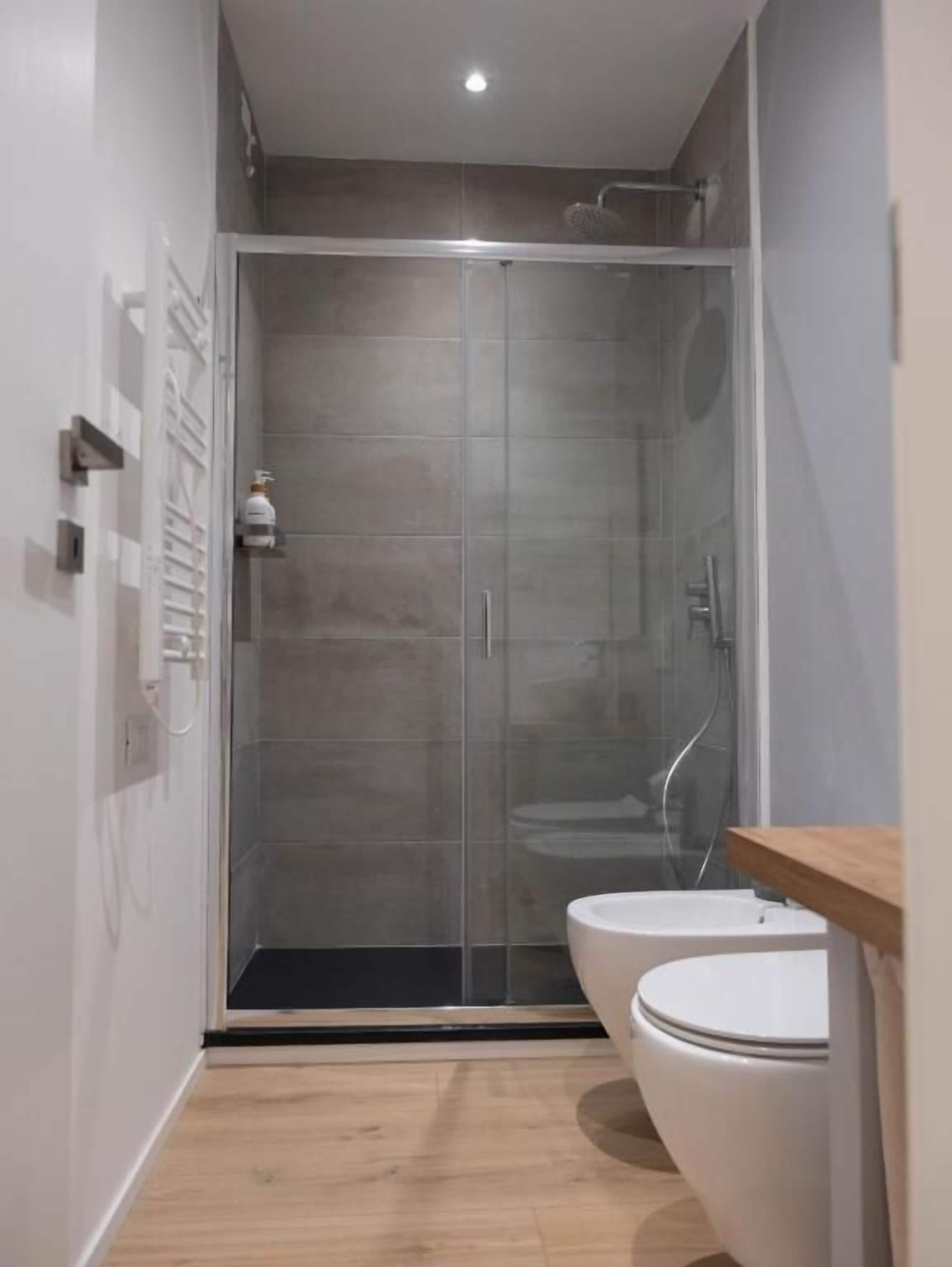 A modern bathroom with a glass shower enclosure, a white toilet, and a wooden vanity.
