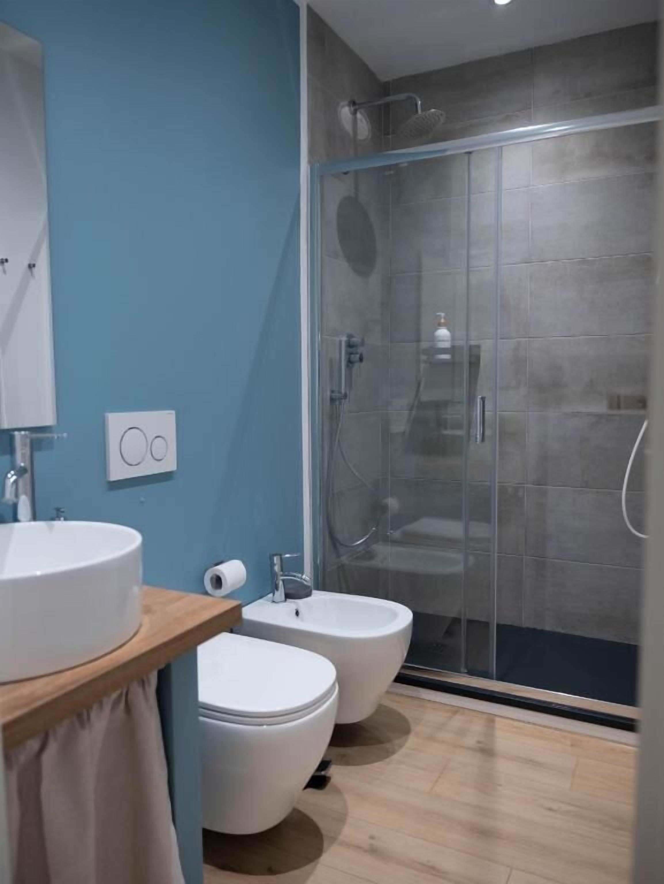 A modern bathroom with a glass shower enclosure, a sink, a bidet, and a toilet.
