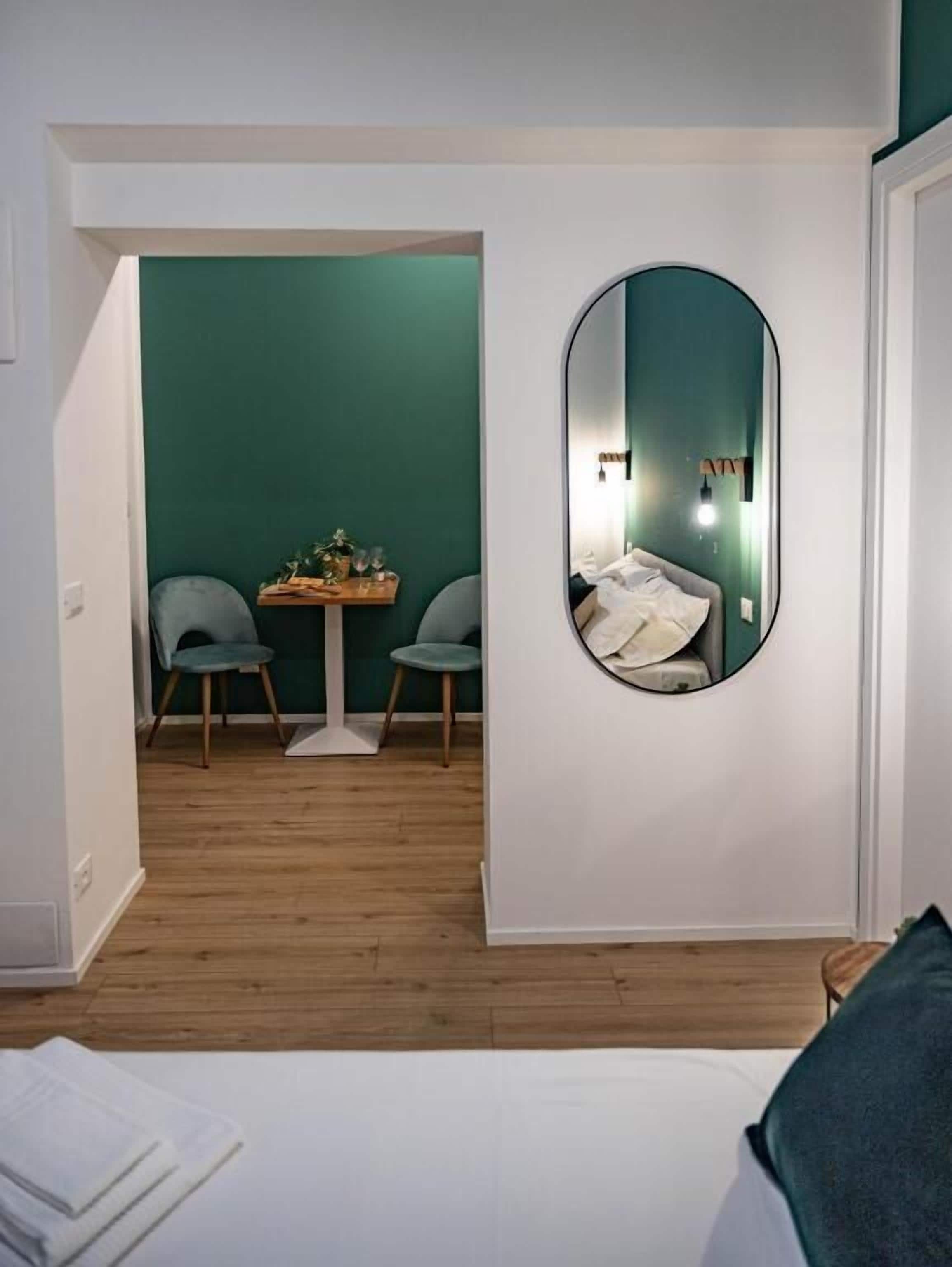 Une pièce avec un lit, un miroir rond, une table avec des chaises et un mur vert.