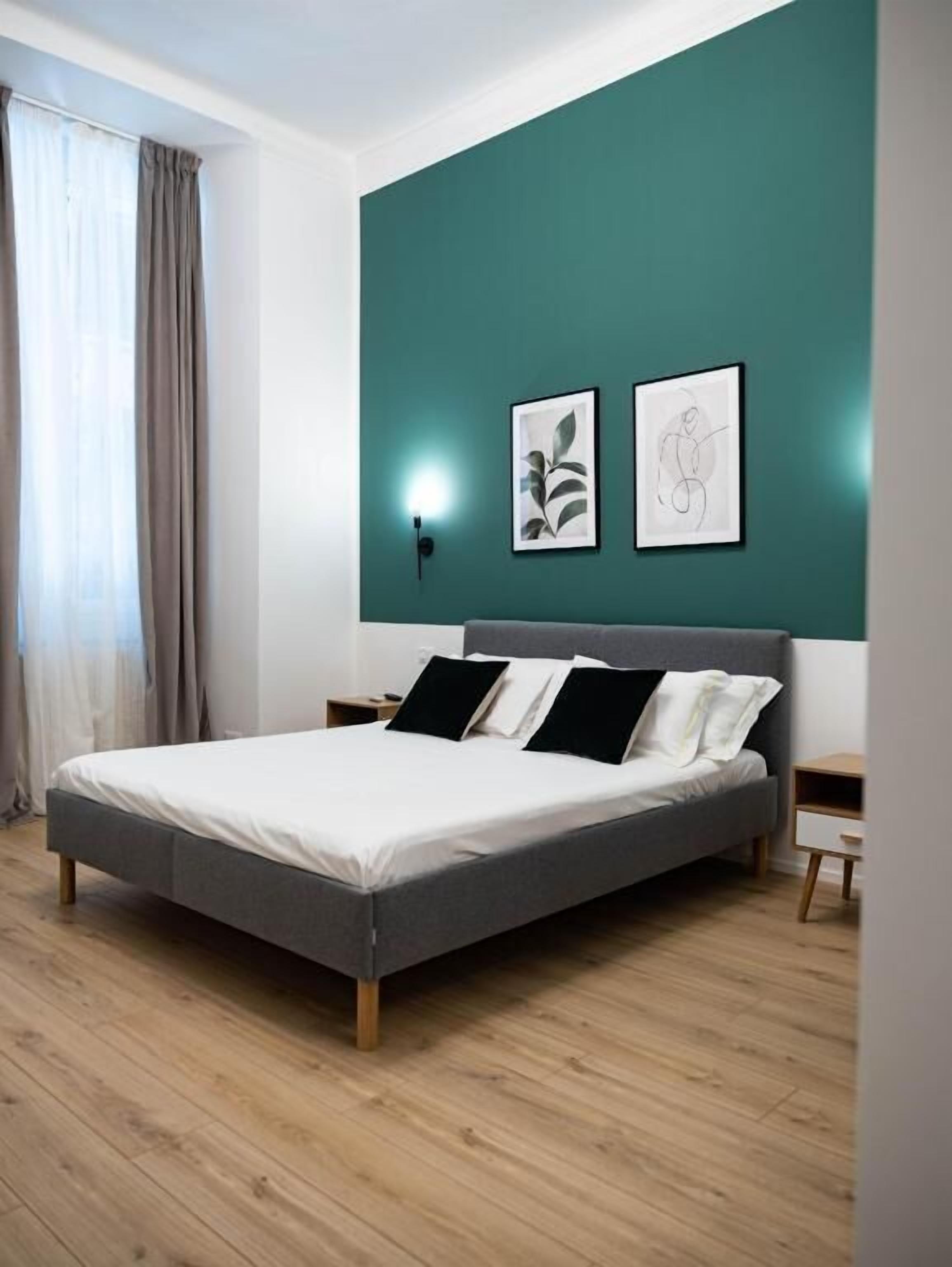 A modern bedroom with a bed, a nightstand, a wall-mounted light, and two framed artworks.
