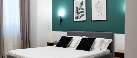 Un dormitorio moderno con una cama, una mesita de noche, una lámpara de pared y dos obras de arte enmarcadas.