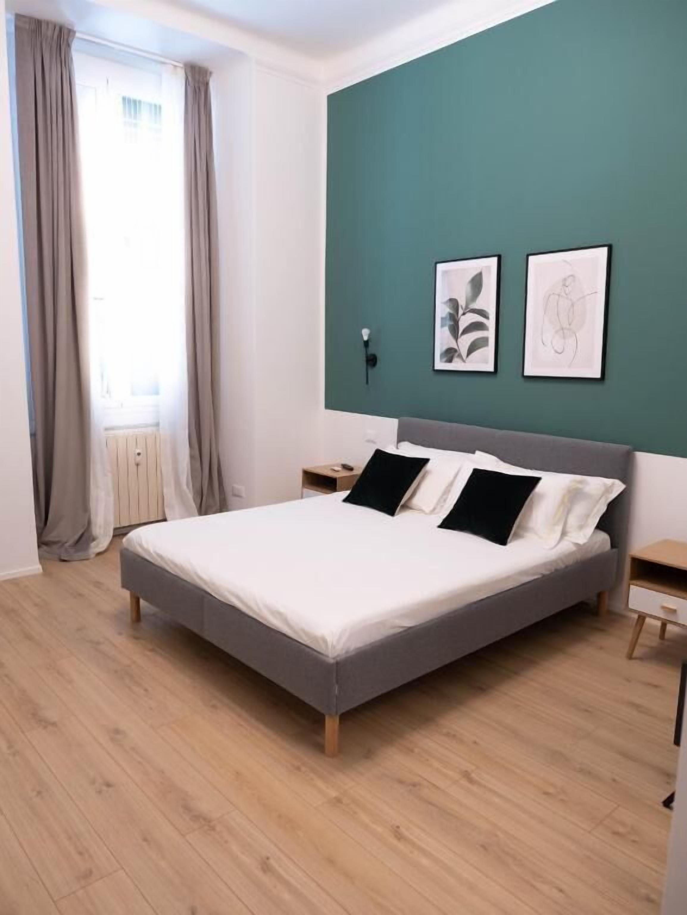 A modern bedroom with a bed, a nightstand, a wall-mounted lamp, and two framed artworks.