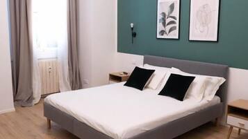 A modern bedroom with a bed, a nightstand, a wall-mounted lamp, and two framed artworks.