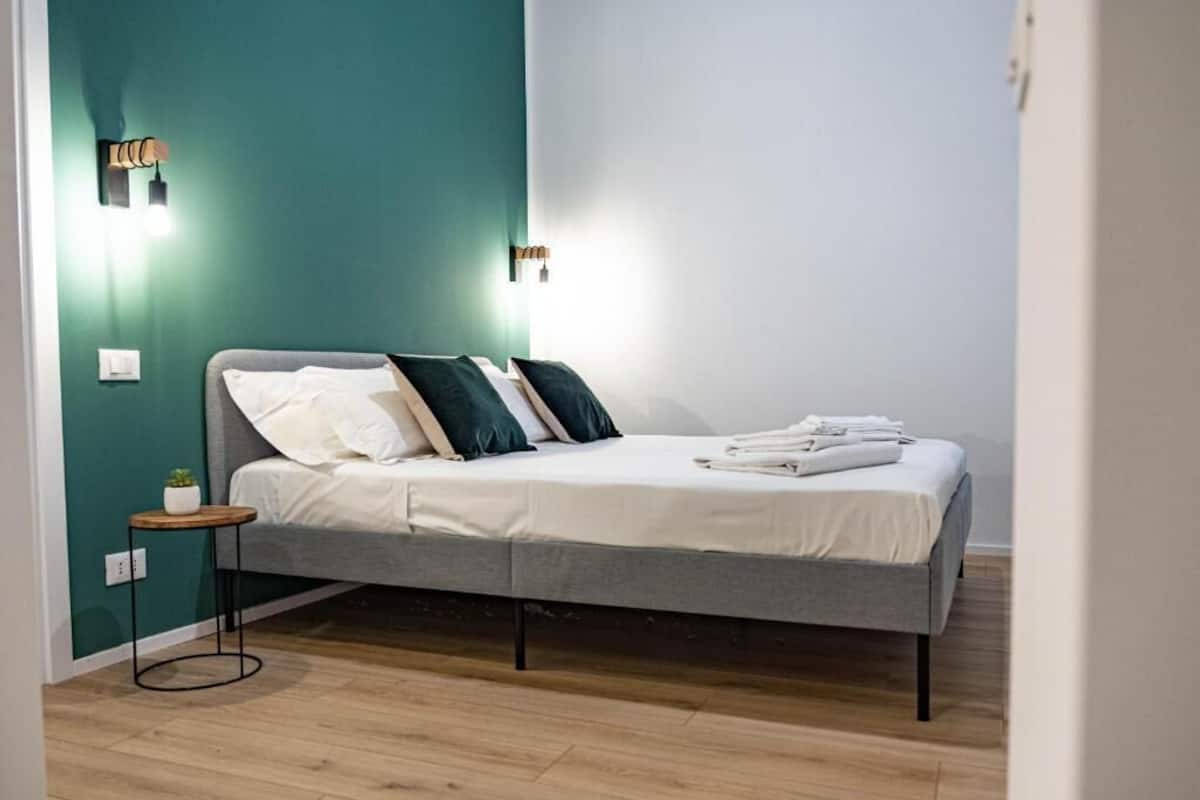 Ein Schlafzimmer mit einem Bett, zwei Wandleuchten, einem kleinen runden Tisch mit einer Pflanze und Holzboden.