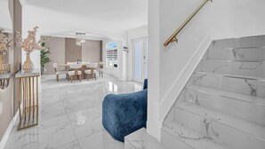 A modern interior with a marble staircase, a dining area, and a blue armchair. - 6BR Villa Tropical Haven Private Pool & BBQ (Homestead)
