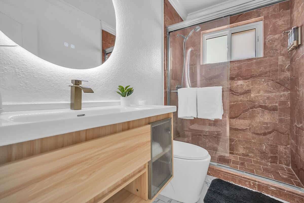 A modern bathroom with a white sink, wooden vanity, a glass shower enclosure, and a marble wall.