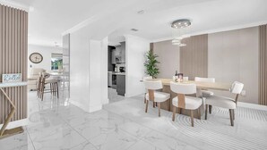 A modern dining area with a marble floor, white furniture, and a chandelier. - 6BR Villa Tropical Haven Private Pool & BBQ (Homestead)