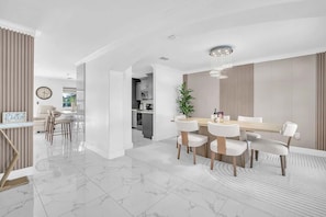 A modern dining area with a marble floor, white furniture, and a chandelier.