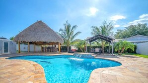 A swimming pool with a thatched-roof structure and a covered seating area. - 6BR Villa Tropical Haven Private Pool & BBQ (Homestead)