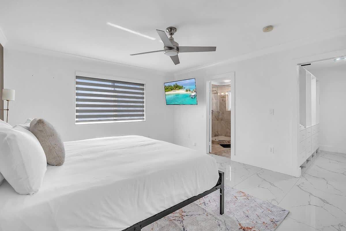A bedroom with a bed, a ceiling fan, a TV, a bathroom door, and a marble floor.
