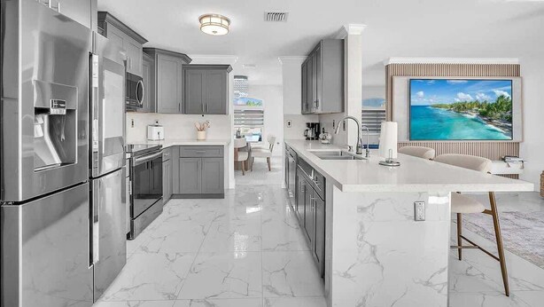A modern kitchen with stainless steel appliances, a marble countertop, and a large island with bar stools. - 6BR Villa Tropical Haven Private Pool & BBQ (Homestead)