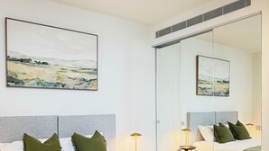 Ett modernt sovrum med en stor säng, ett sängbord, en lampa och en spegel.