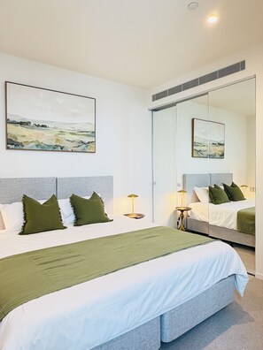 A modern bedroom with a large bed, a bedside table, a lamp, and a mirror. - Panoramic City & Bay Views and Free Parking (Southbank)