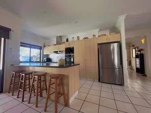 A modern kitchen with wooden cabinets, a stainless steel refrigerator, and a large island with stools.