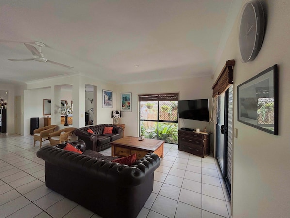 A living room with a black leather sofa, a wooden coffee table, a TV, and a clock on the wall.