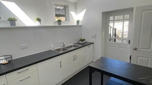 Een moderne keuken met dakramen, een zwart aanrecht, witte kasten en een deur naar buiten.