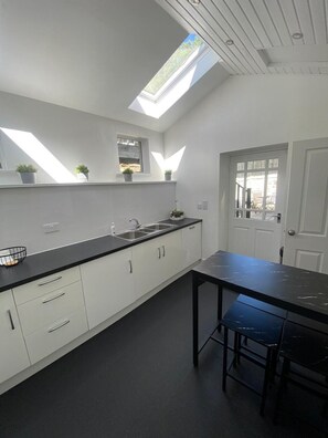A modern kitchen with skylights, a black countertop, white cabinets, and a door leading outside. - High Street House Sleeps 4 With Parking (Biggar)