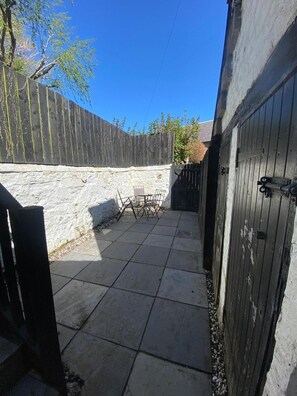 A paved patio with a table and chairs, a stone wall, and a wooden fence. - High Street House Sleeps 4 With Parking (Biggar)