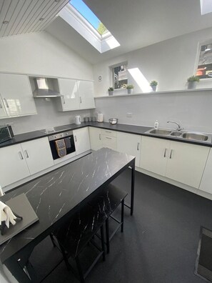 Una cocina moderna con tragaluz, armarios blancos, encimera negra y comedor con mesa y sillas.