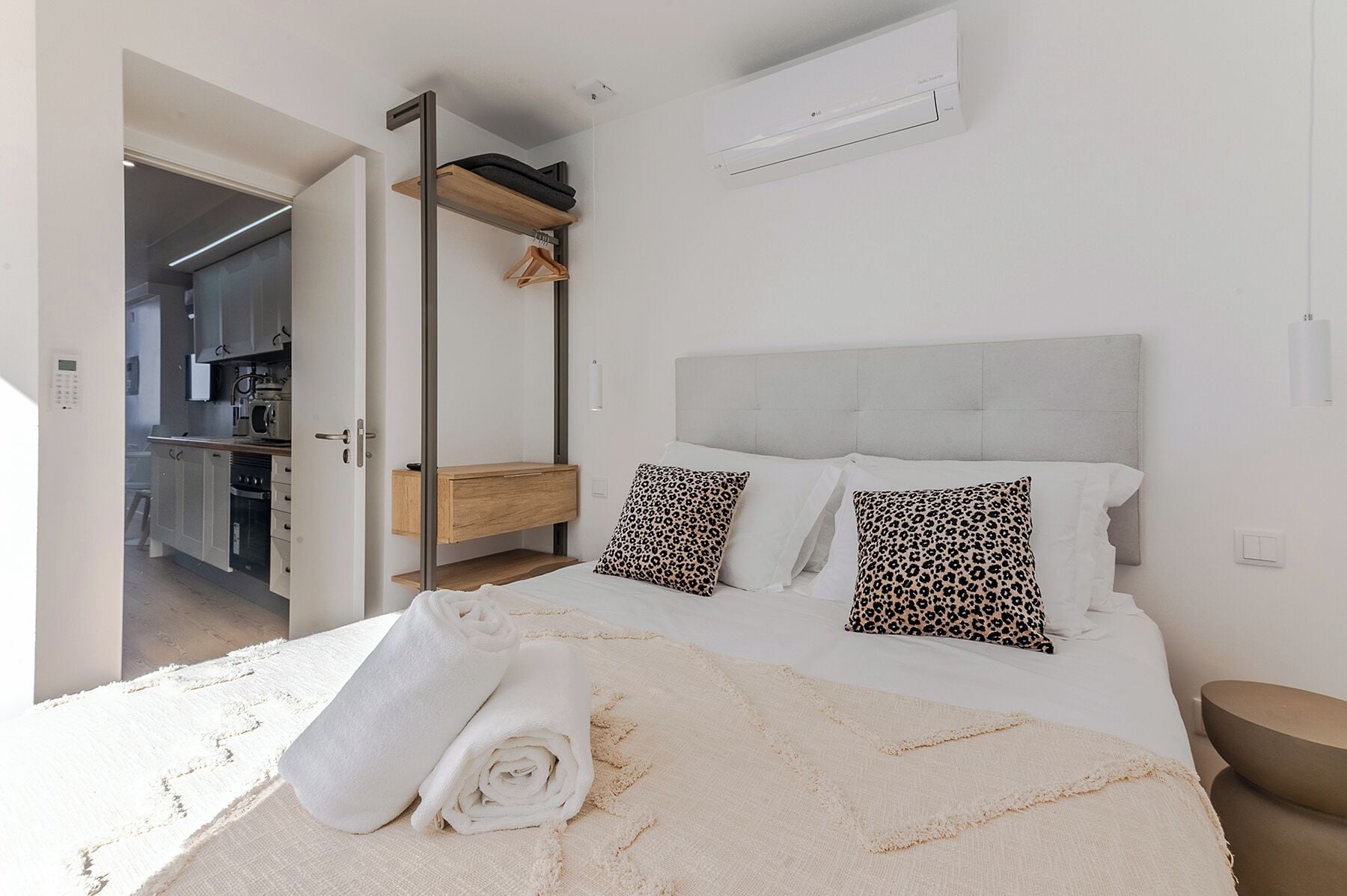 A bedroom with a bed, pillows, a towel, a wardrobe, and an air conditioning unit.