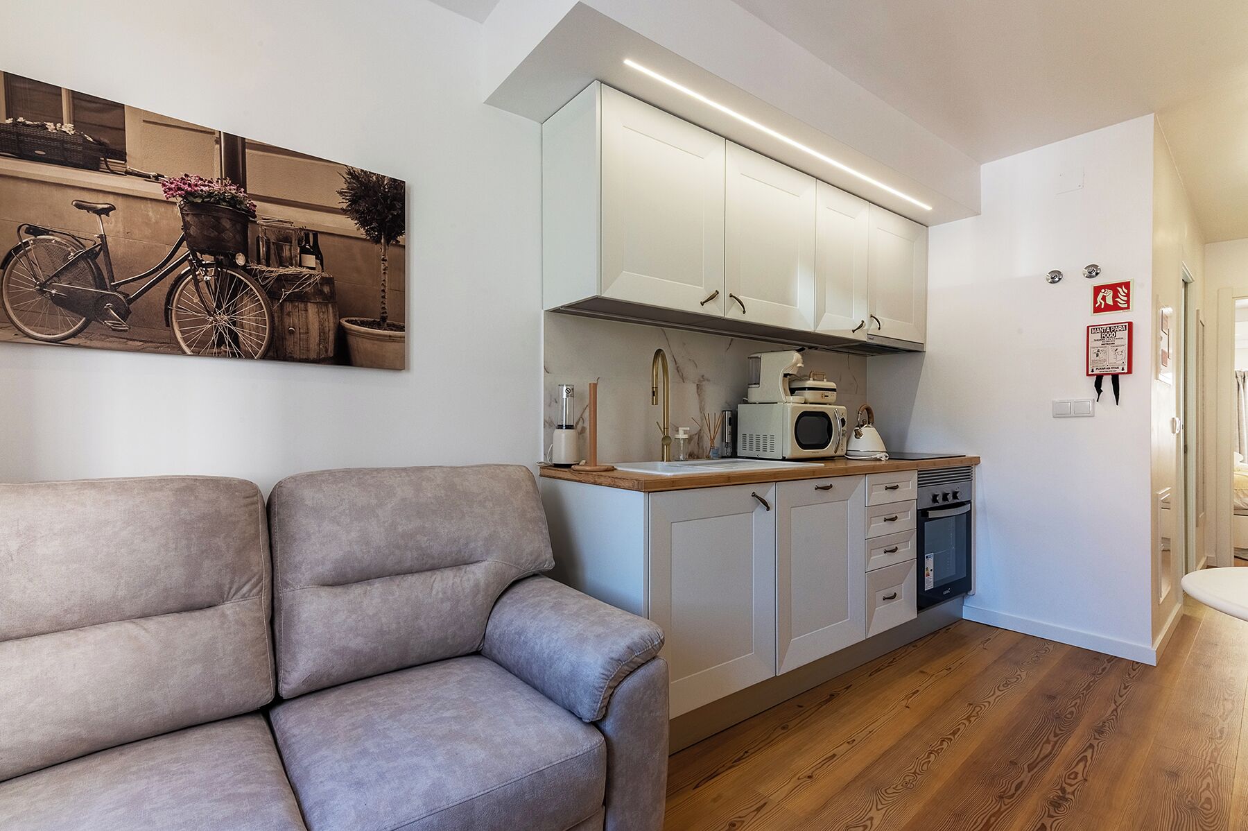 A compact kitchen with white cabinets, a wooden countertop, and a built-in microwave.