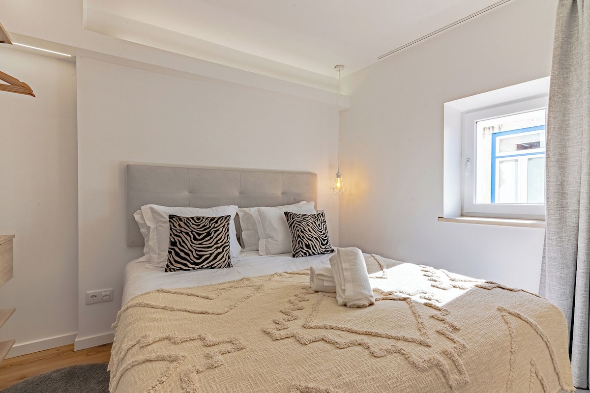 Quarto com cama, janela e luminária fixada na parede.