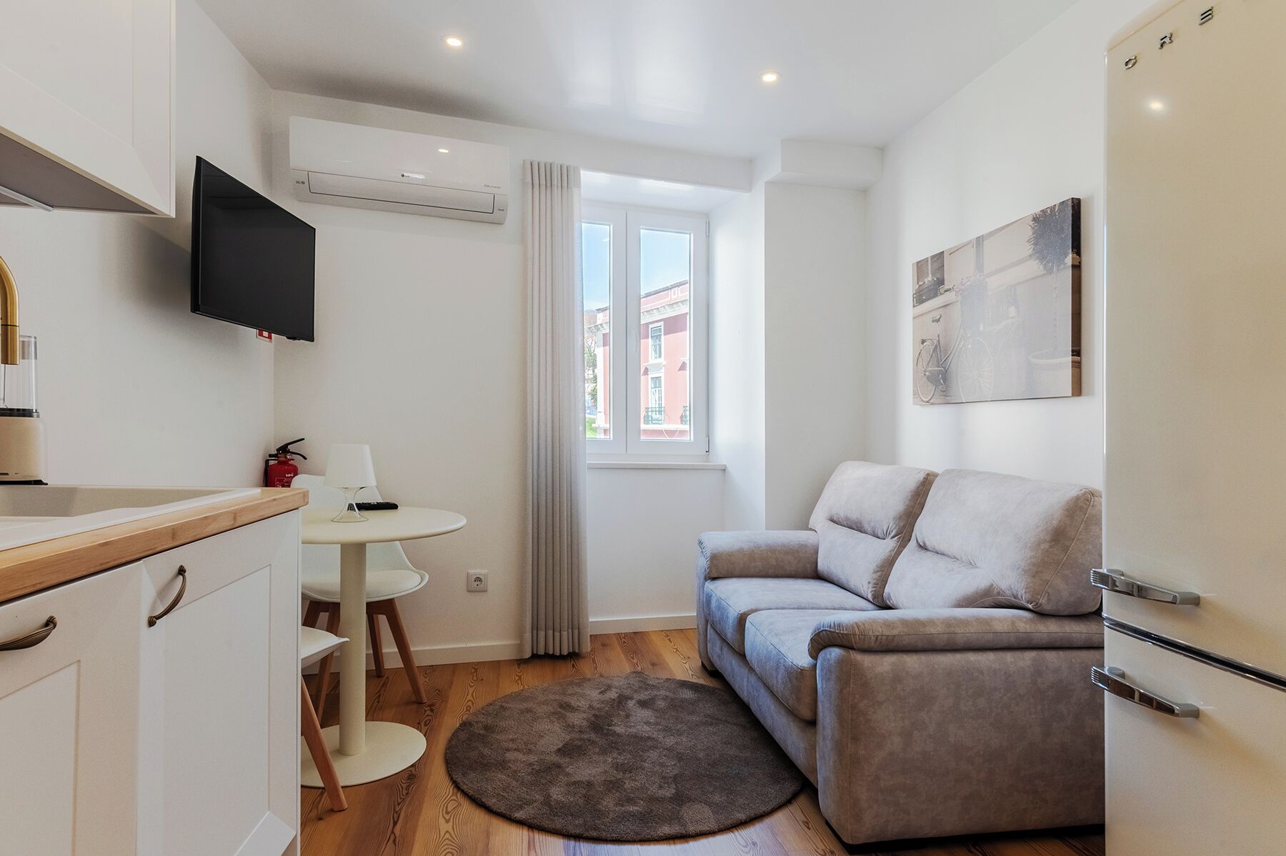 A compact living space with a kitchenette, a sofa, a small table, and a TV.