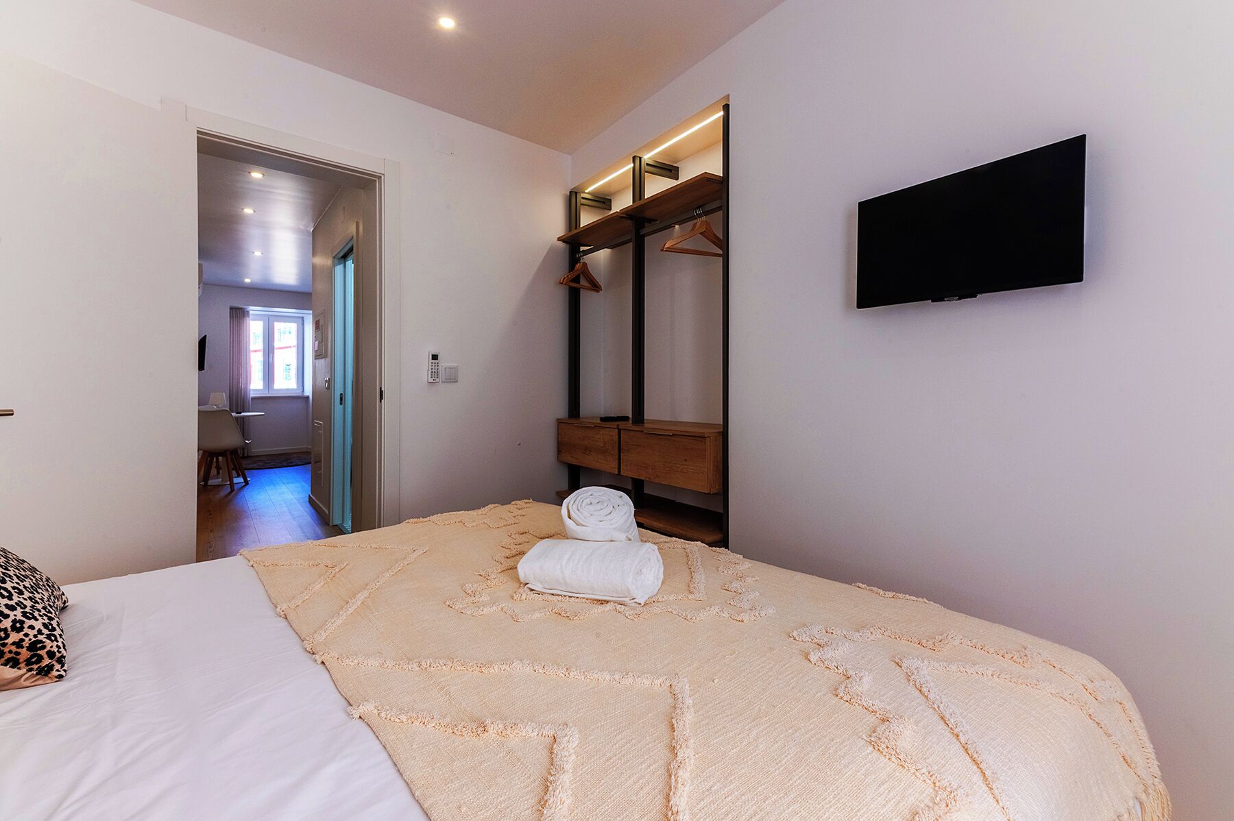 Une chambre à coucher avec un lit, un téléviseur fixé au mur, une commode en bois et un miroir.