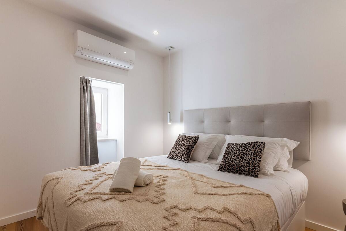 Quarto com cama, ar condicionado e janela com cortinas.