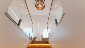 A modern staircase with wooden steps and glass railings, leading to a room with a view. - White Angels by Portas do Sol Apartments (Lisbon)