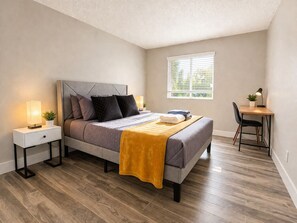 A bedroom with a bed, bedside tables, a desk, and a window.