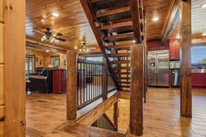 Interior em madeira com escada, cozinha com eletrodomésticos de aço inoxidável e área de estar com sofá e mesa de centro.