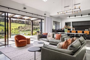 A modern living room with a sofa, armchairs, and a dining area with a view of the outdoors. - MAGNIFICENT AND OPULENT 5 BEDROOM OASIS BOASTING SWEEPING VALLEY VIEWS (Yallingup)
