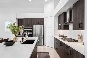 A modern kitchen with dark wood cabinets, stainless steel appliances, and a white marble countertop. - 4 Bedroom Luxury Estate With Pool Spa Firepit (Indio)