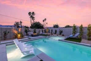 A swimming pool with lounge chairs and a fire pit, surrounded by a landscaped garden and a view of palm trees and mountains. - 4 Bedroom Luxury Estate With Pool Spa Firepit (Indio)